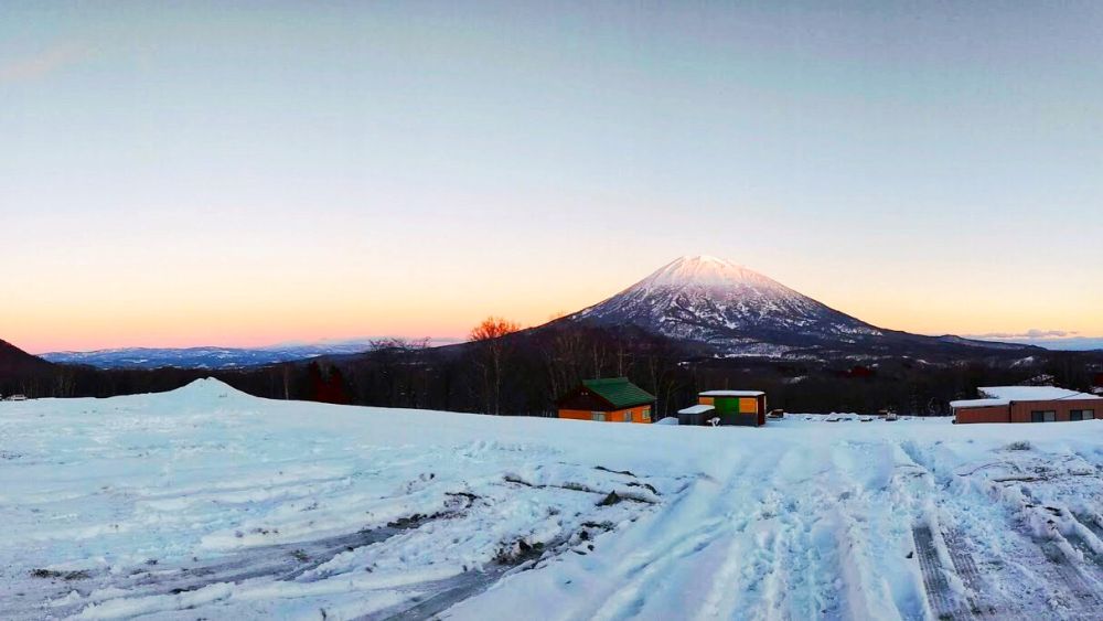 Niseko secret viewpoint snowy sunset, Mount Yotei and colorful cabins in the distance
